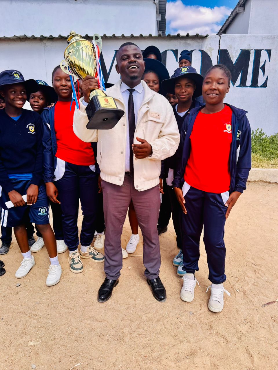 Twin One Academy students celebrating beside a coach holding a trophy